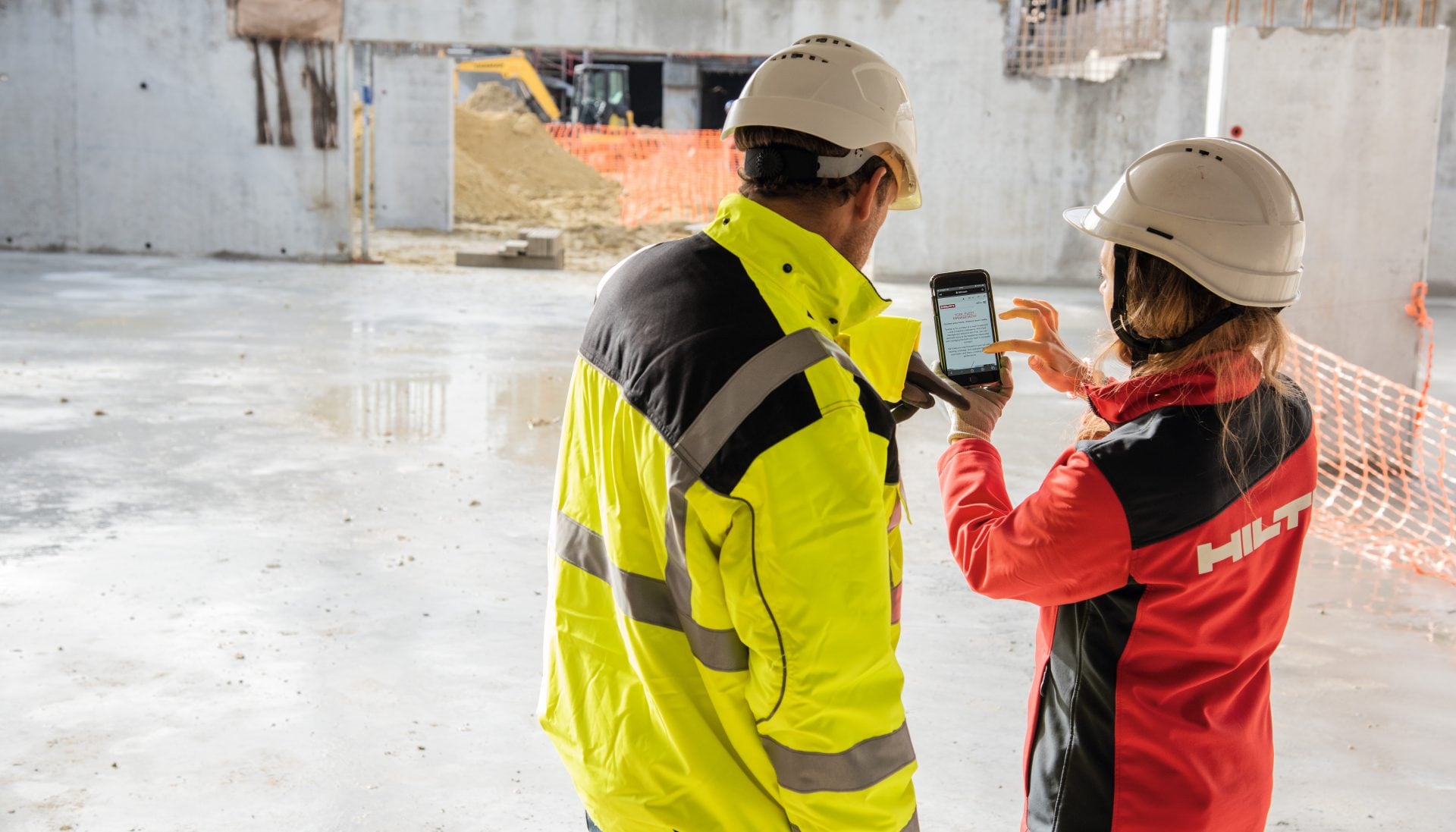Dva pracovníci na stavbě spolu koukají do mobilu